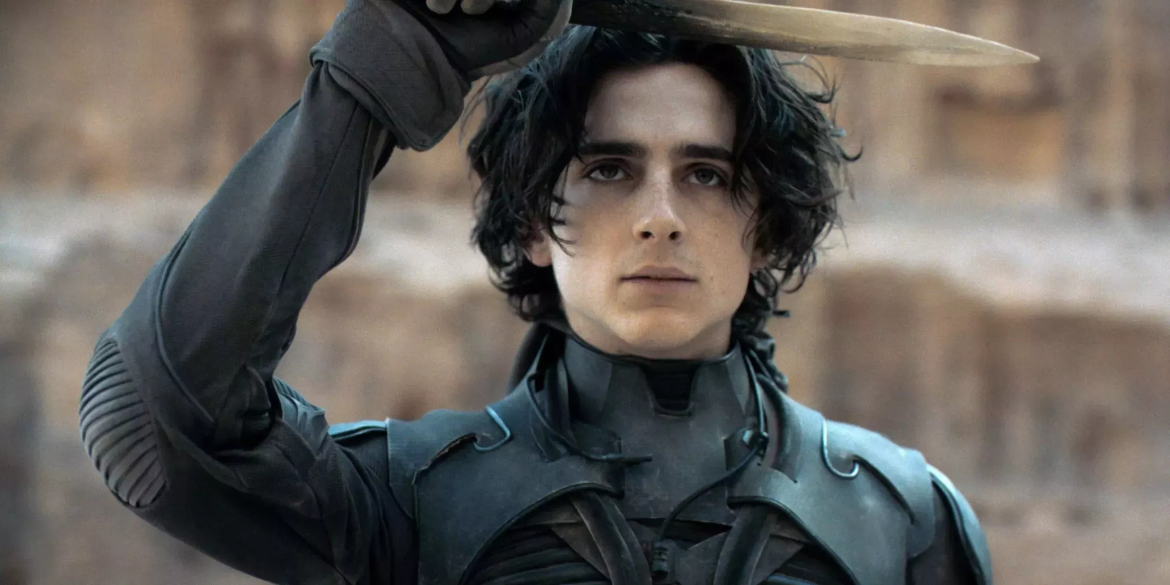 Timothée Chalamet as Paul Atreides holds a dagger above his head in Dune