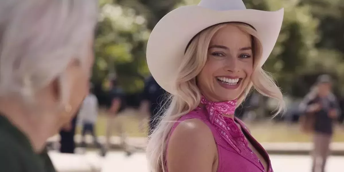 Margot Robbie smiling in a cowgirl hat as Barbie on the bench with the old woman