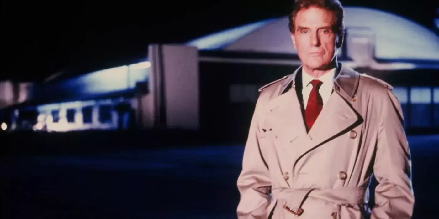 Robert Stack standing to the side with his hands on his trench coat in Unsolved Mysteries