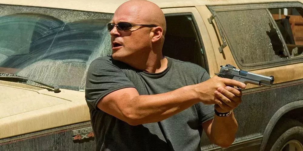 Detective Vic Mackey from The Shield holding a firearm and standing next to a car