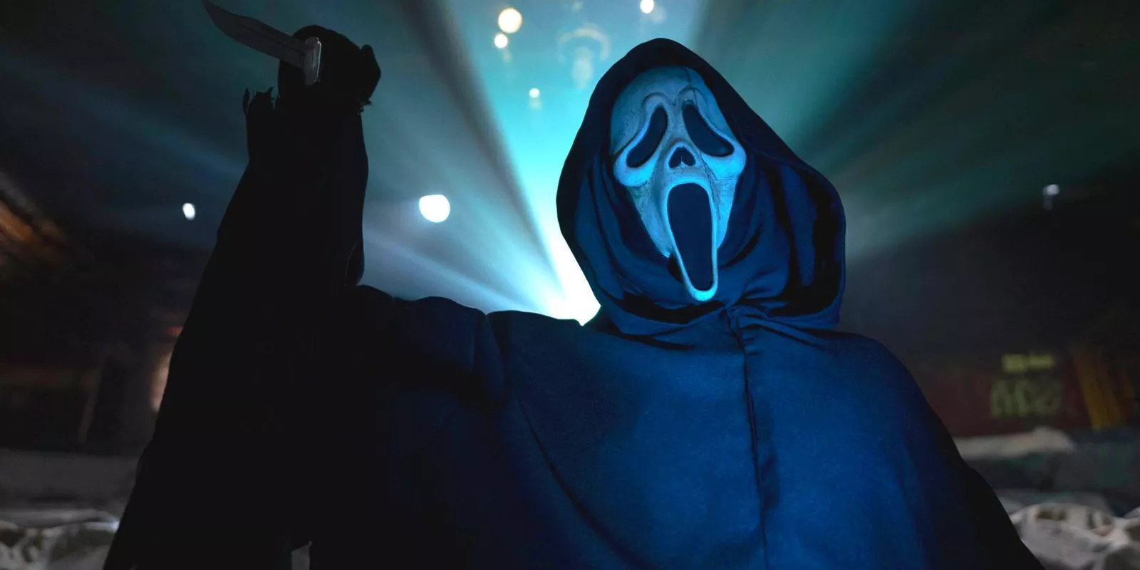 Ghostface en un cine, sosteniendo un cuchillo mientras la luz del proyector brilla sobre él