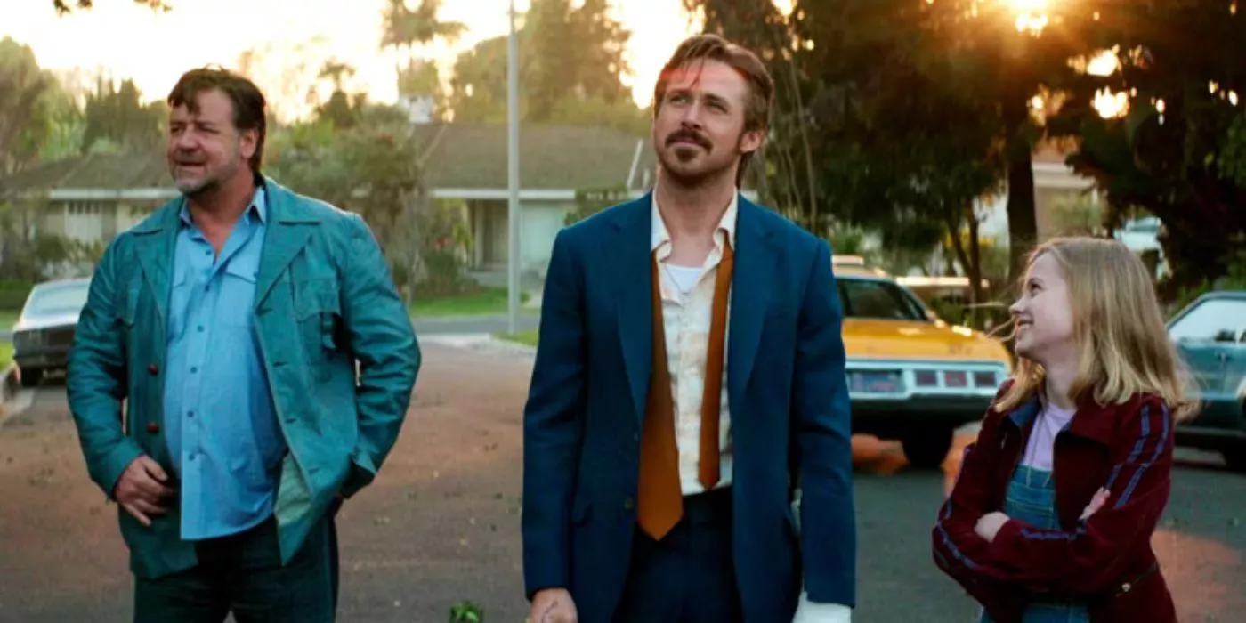 Ryan Gosling, Russell Crowe, and Angourie Rice stand outside on the street, smiling in The Nice Guys.